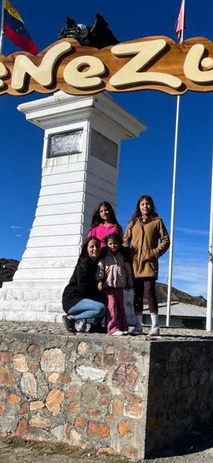 Family in front of a wooden VENEZUELA sign at altitude